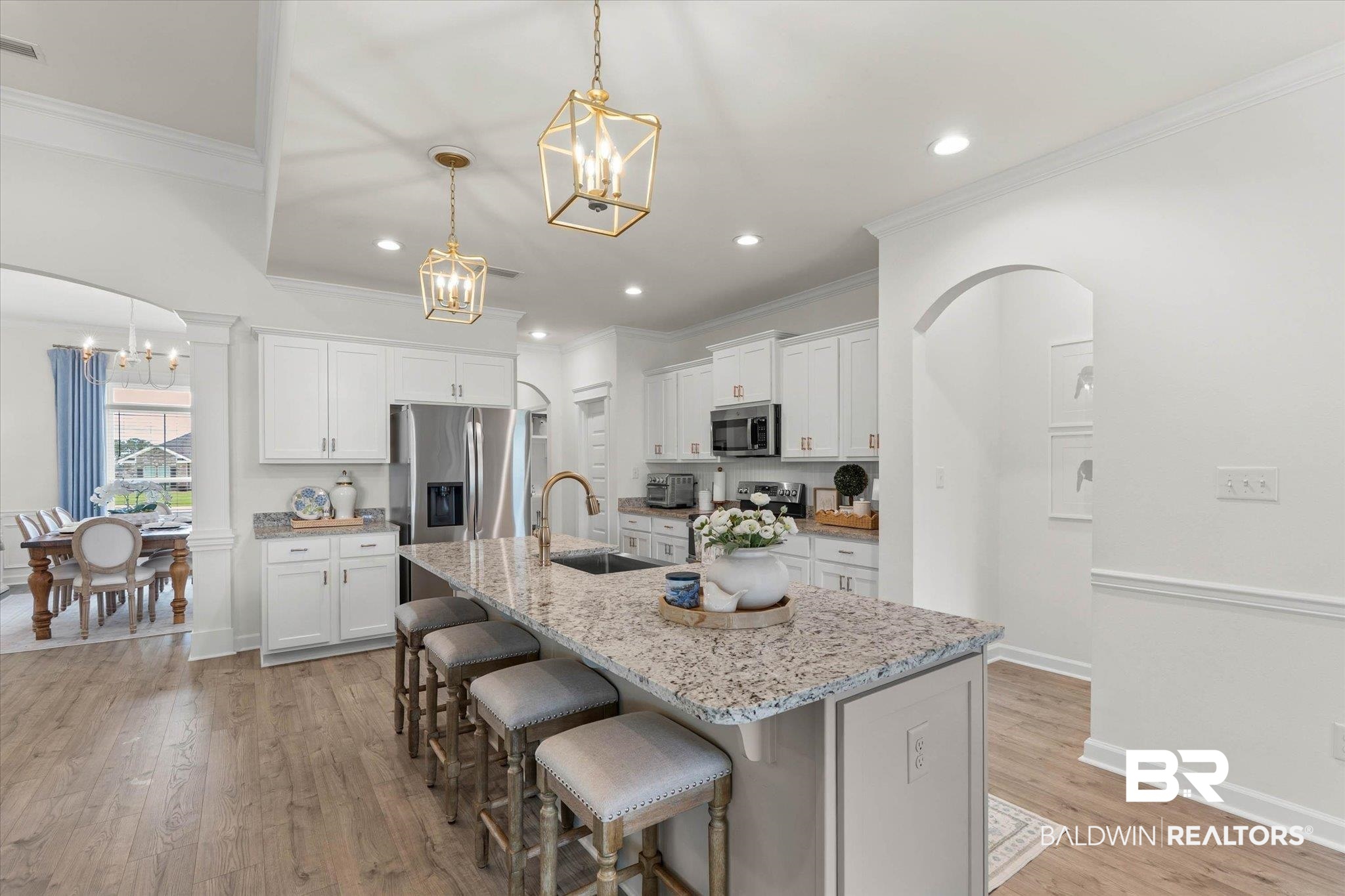 9074 Moses Way Theodore, AL 36582 - Photo 17 of 52 Open-concept kitchen featuring an oversized island with granite countertops, stainless steel appliances, white cabinetry, and wood-finish flooring