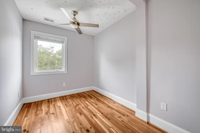 a view of empty room with wooden floor and fan
