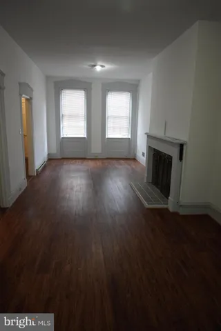 an empty room with wooden floor fireplace and windows