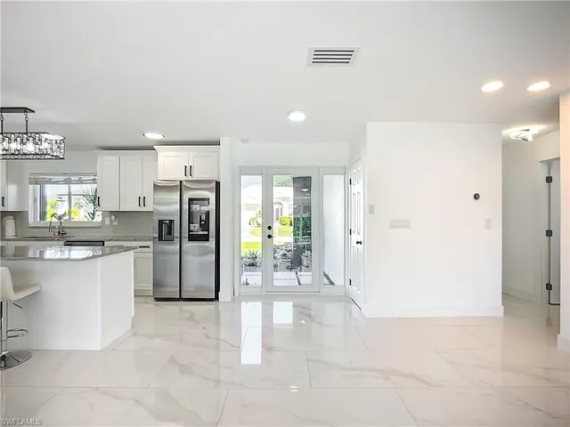 a large white kitchen with stainless steel appliances kitchen island granite countertop a refrigerator and a sink