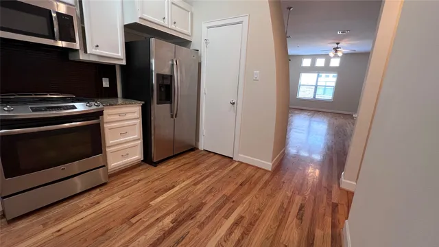 a view of a kitchen from an empty room with wooden floor and a kitchen