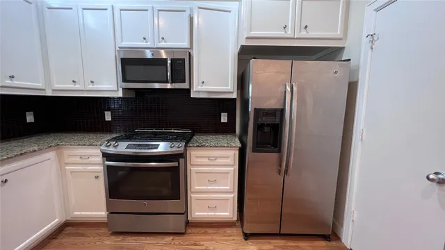 a kitchen with stainless steel appliances granite countertop a refrigerator stove and white cabinets