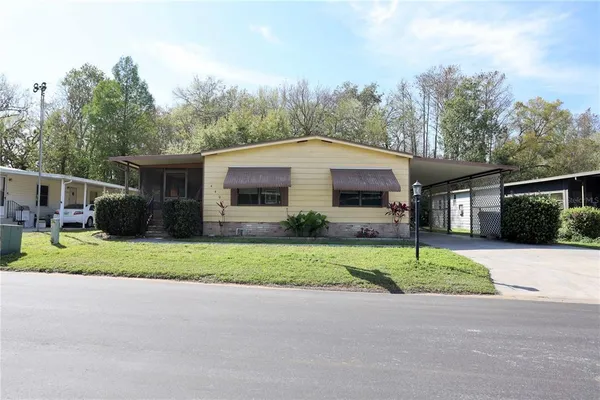 a yellow house with a big yard plants and big trees