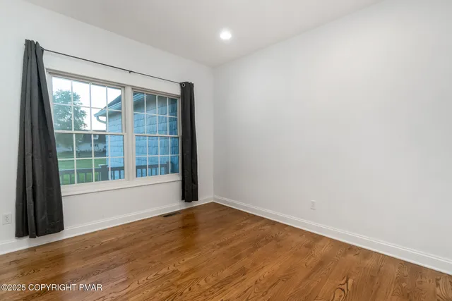 an empty room with wooden floor chandelier fan and windows
