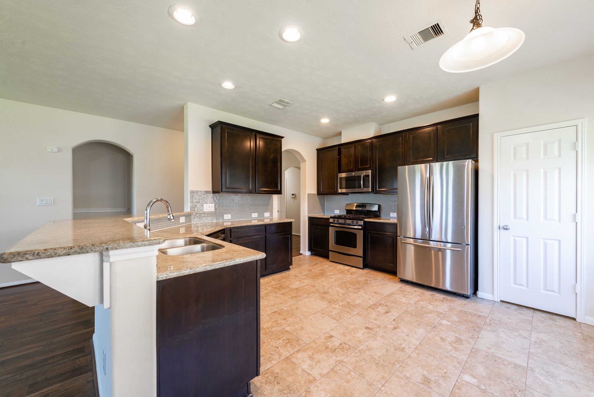 26302 Fox Ridge Lane Katy, TX 77494 - Photo 15 of 35 The family kitchen featuring modern stainless steel appliances, dark cabinetry, and a convenient breakfast bar with elegant tile flooring and recessed lighting.