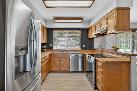 a kitchen with stainless steel appliances granite countertop a refrigerator a sink dishwasher a stove and a dining table with wooden floor