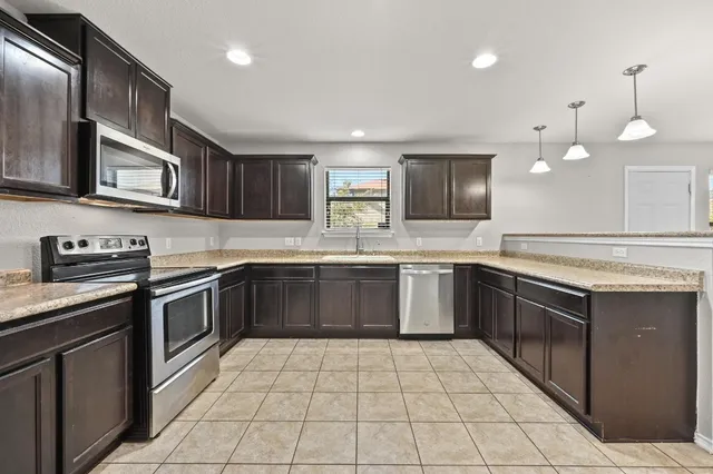 a large kitchen with stainless steel appliances granite countertop a stove top oven a sink dishwasher and a refrigerator with wooden cabinets