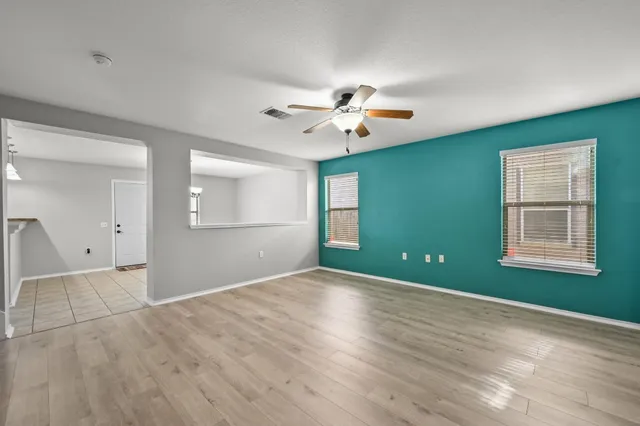 an empty room with wooden floor chandelier fan and windows