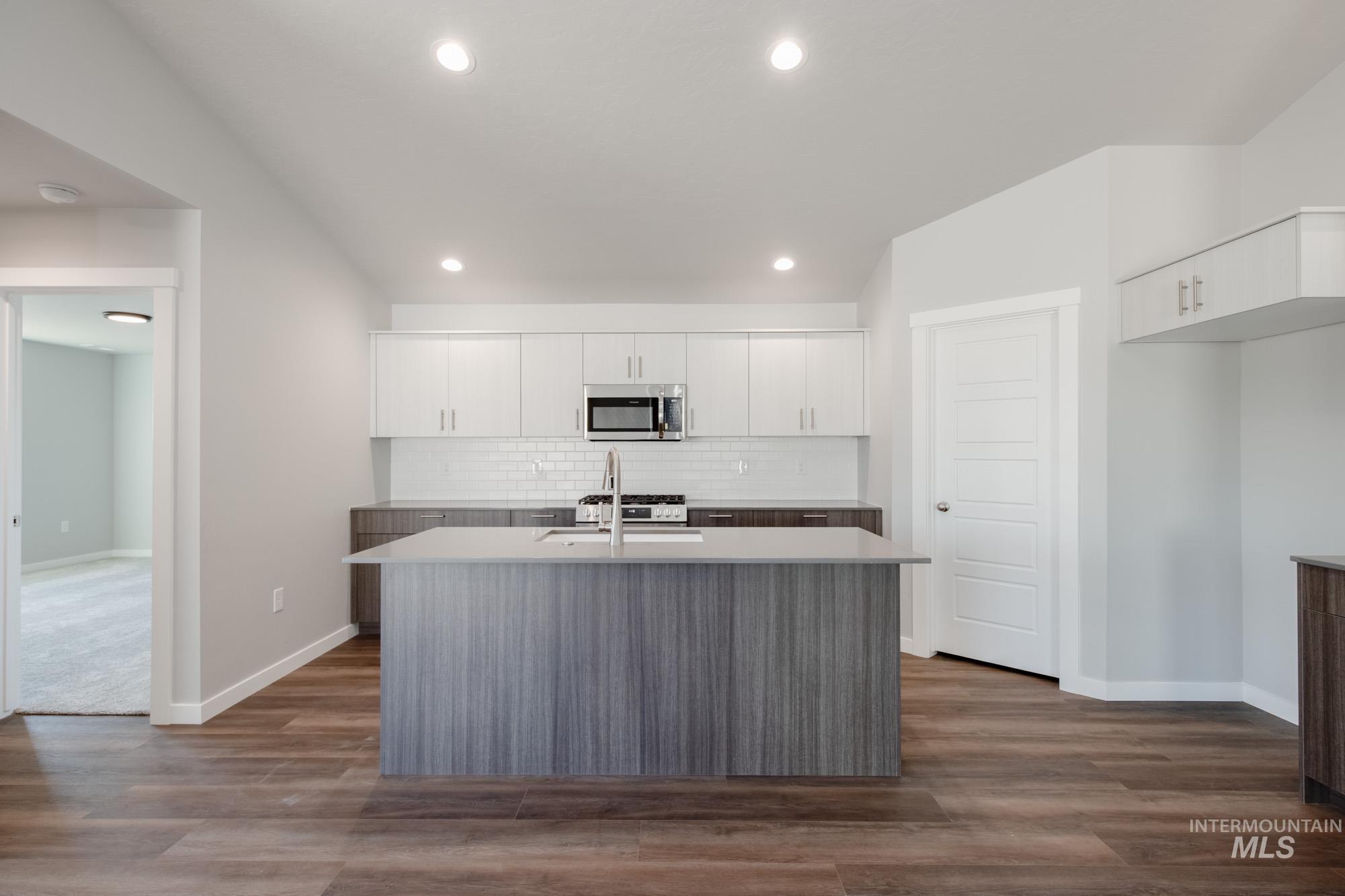 2940 North Schimigadoon Way Eagle, ID 83616 - Photo 3 of 21 Kitchen featuring an island with sink, white cabinets, backsplash, stainless steel microwave, and dark wood finished floors
