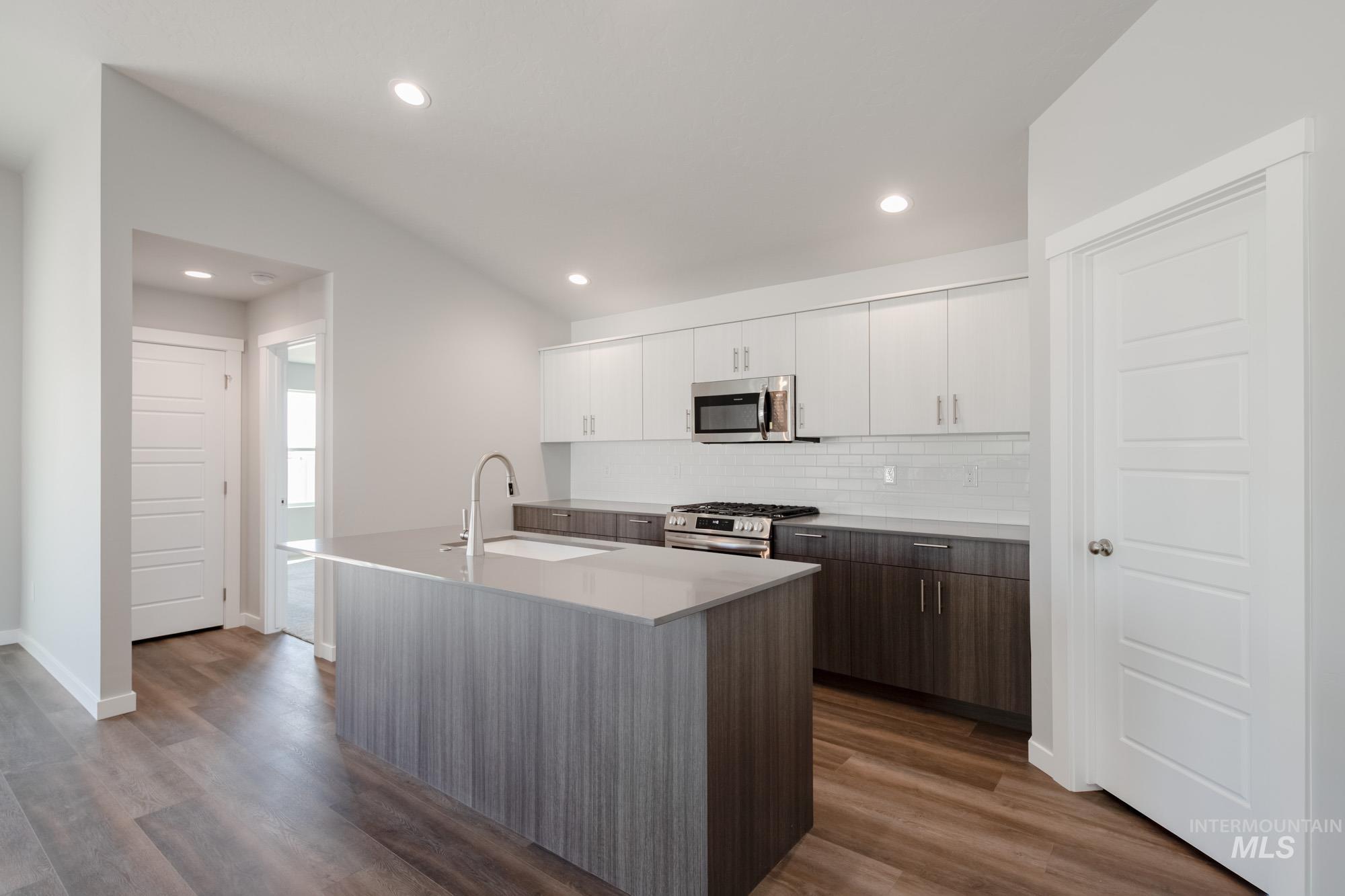2940 North Schimigadoon Way Eagle, ID 83616 - Photo 4 of 21 Kitchen featuring white cabinets, a kitchen island with sink, backsplash, appliances with stainless steel finishes, and dark wood-style flooring