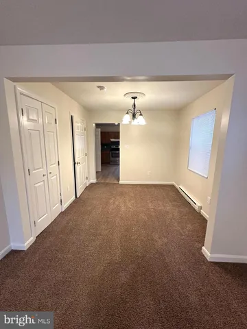 an empty room with a chandelier fan and kitchen view