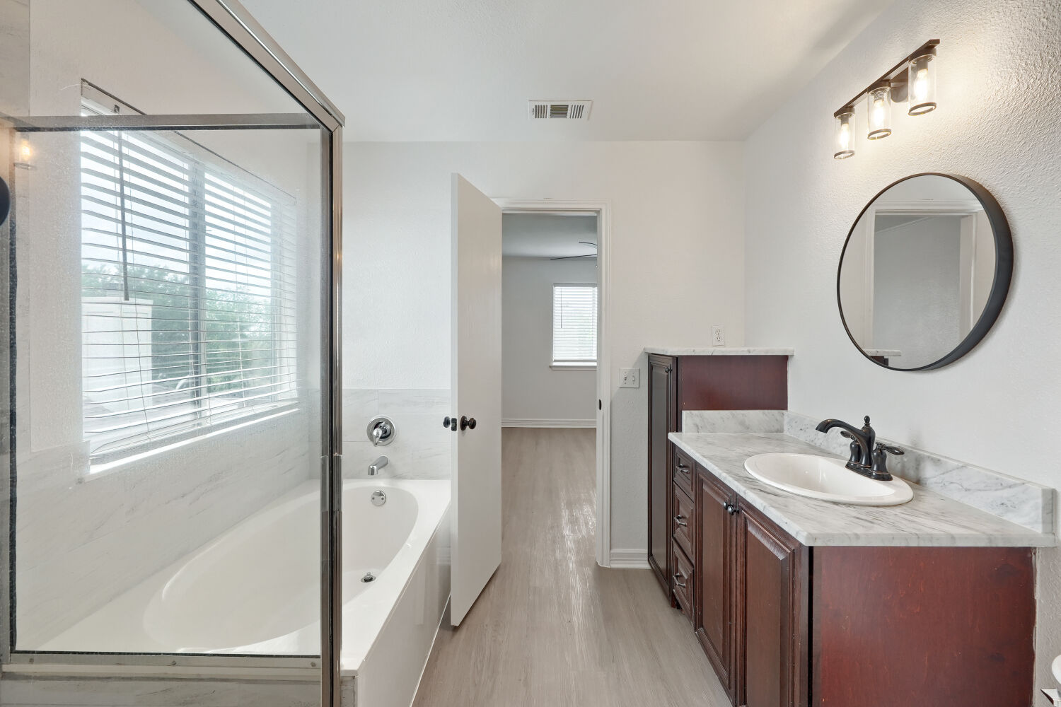 184 Unity Kyle, TX 78640 - Photo 7 of 11 Bathroom featuring a bathtub with a shower enclosure, a vanity with a sink and dark wood cabinetry, and a circular mirror