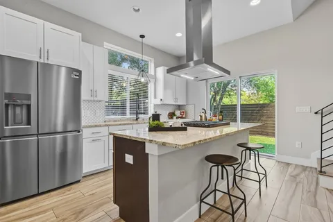 a kitchen with stainless steel appliances granite countertop a refrigerator a sink dishwasher a stove and white cabinets with wooden floor