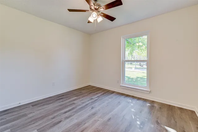 an empty room with wooden floor chandelier fan and windows