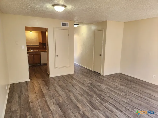 a view of empty room with wooden floor and kitchen