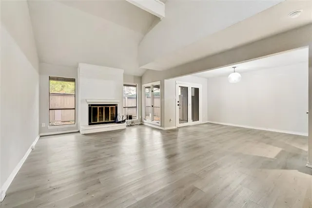 an empty room with wooden floor fireplace and windows