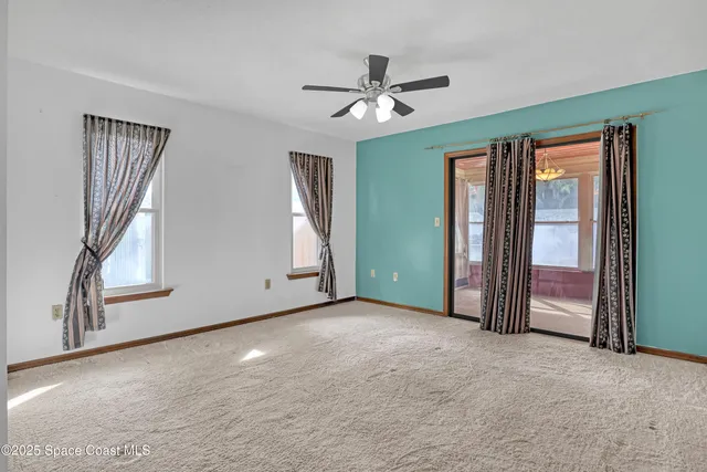 an empty room with a chandelier fan and windows