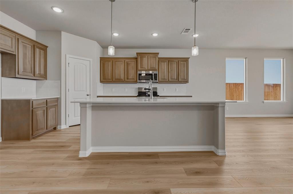 1201 Colca Drive Springtown, TX 76082 - Photo 11 of 32 Kitchen featuring wood-finish cabinetry, a large center island with a sink, stainless steel appliances, and a tile backsplash