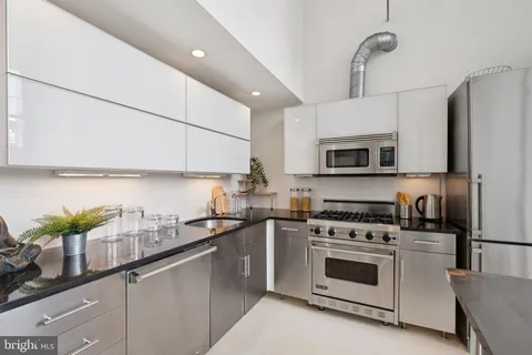 a kitchen with stainless steel appliances white cabinets a sink a stove a microwave a refrigerator and cabinets