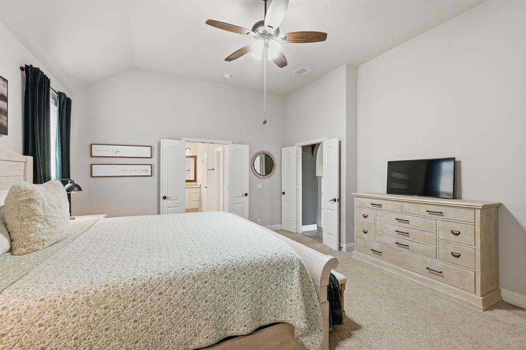 924 Timber Ridge Drive Justin, TX 76247 - Photo 19 of 32 Carpeted bedroom featuring a vaulted ceiling with a ceiling fan, light-colored walls, and double doors opening to an adjoining bathroom