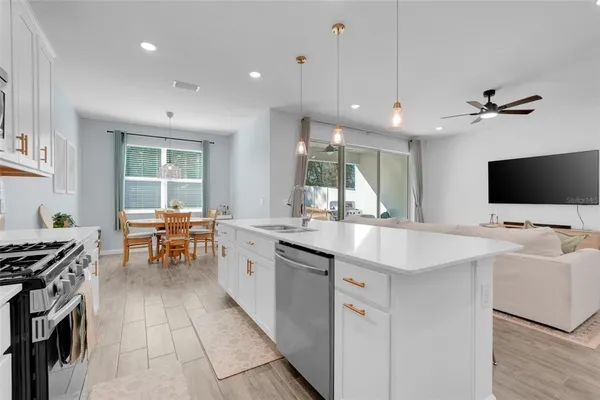 a kitchen with stainless steel appliances a stove top oven a sink a dining table and chairs with wooden floor
