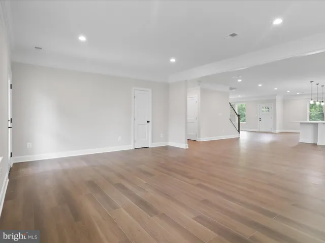 a view of an empty room with wooden floor kitchen view and a window