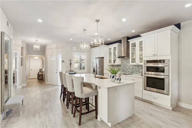 a large white kitchen with stainless steel appliances kitchen island granite countertop a dining table chairs and white cabinets