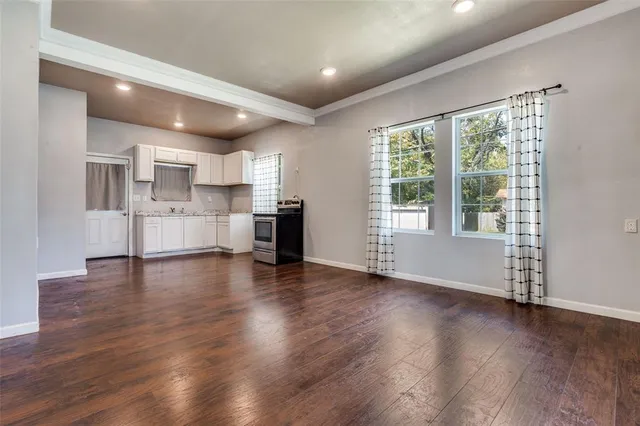 a view of empty room with wooden floor and kitchen view