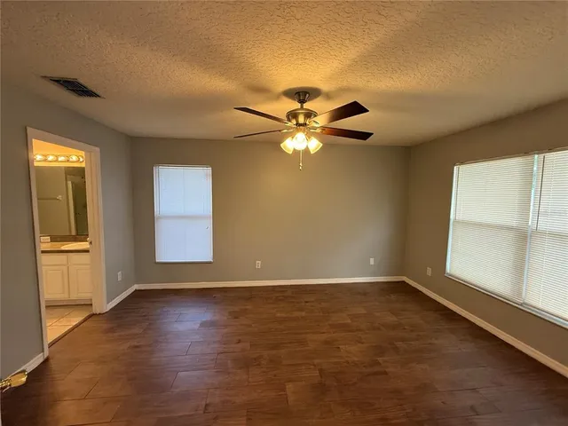 an empty room with wooden floor chandelier fan and windows