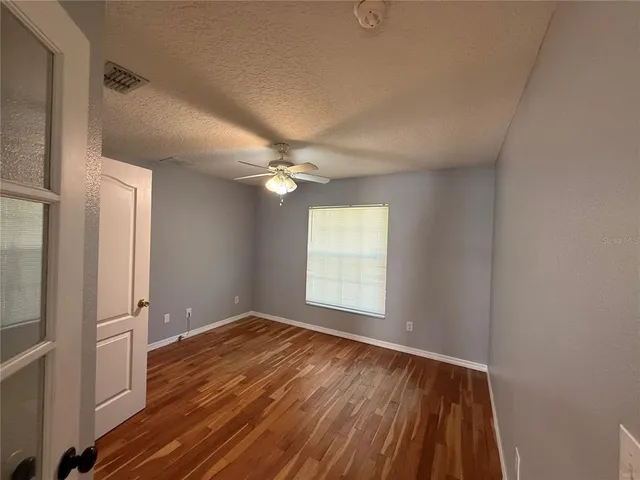 a view of empty room with wooden floor and fan