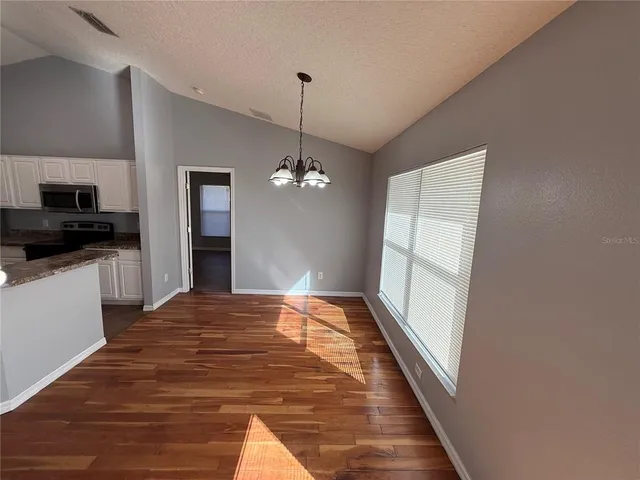 a view of empty room with wooden floor and kitchen view