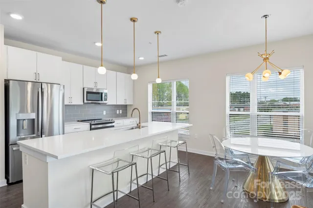 a kitchen with stainless steel appliances granite countertop a stove a refrigerator a kitchen island a dining table and chairs