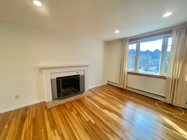 a view of an empty room with wooden floor fireplace and a window