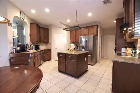 a large kitchen with stainless steel appliances granite countertop a refrigerator a sink dishwasher a oven and a dining table with wooden floor