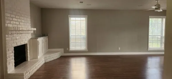 an empty room with wooden floor fireplace and windows