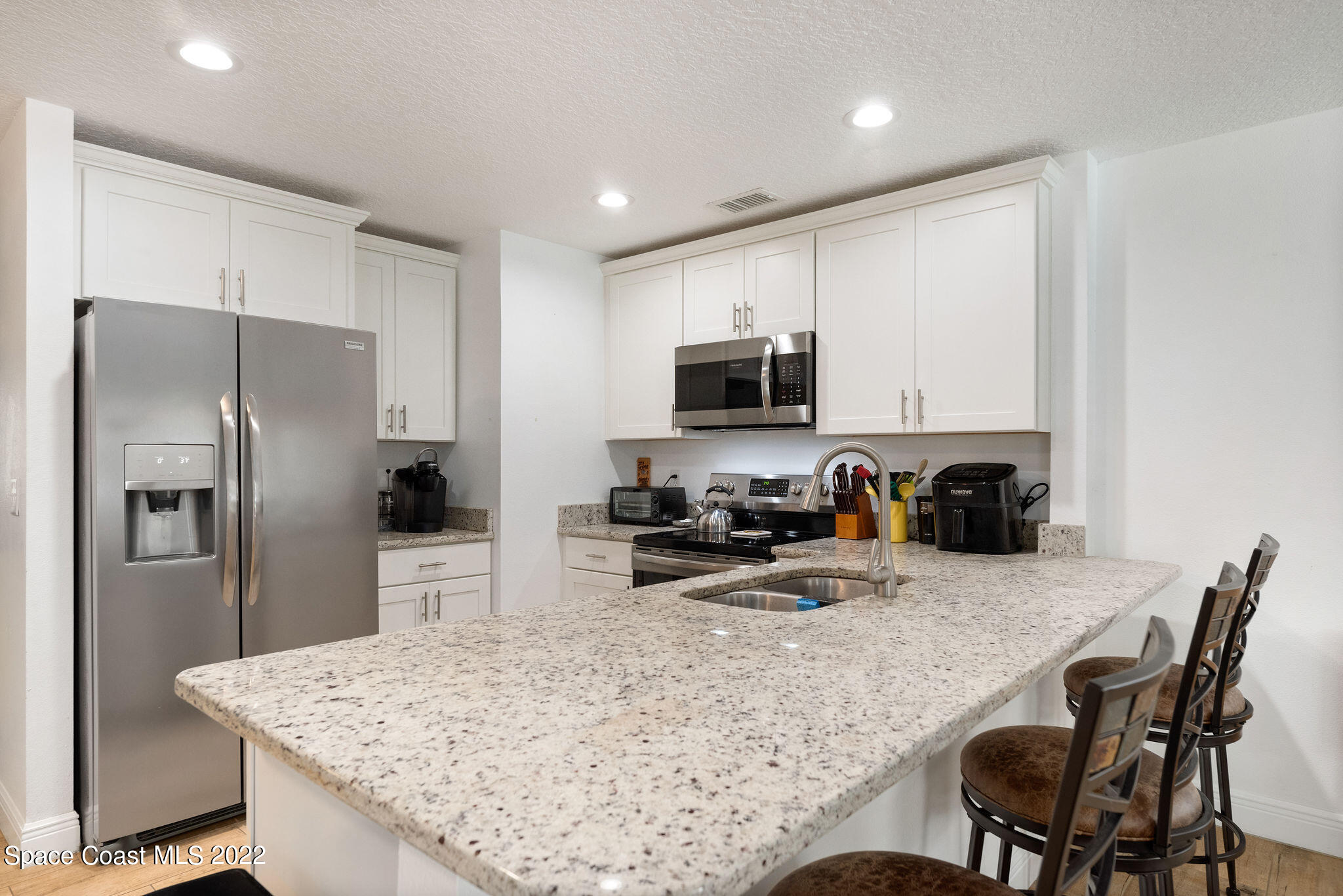 1821 Britt Road Cocoa, FL 32926 - Photo 18 of 63 a kitchen with stainless steel appliances granite countertop a sink a stove a microwave a refrigerator and white cabinets with wooden floor