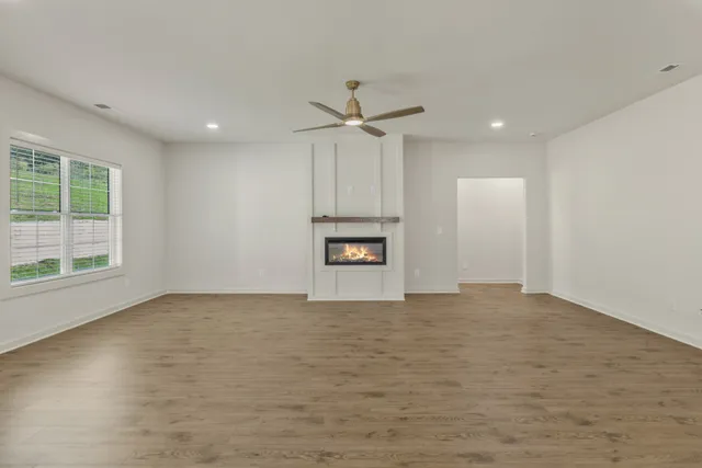 an empty room with wooden floor ceiling fan and windows