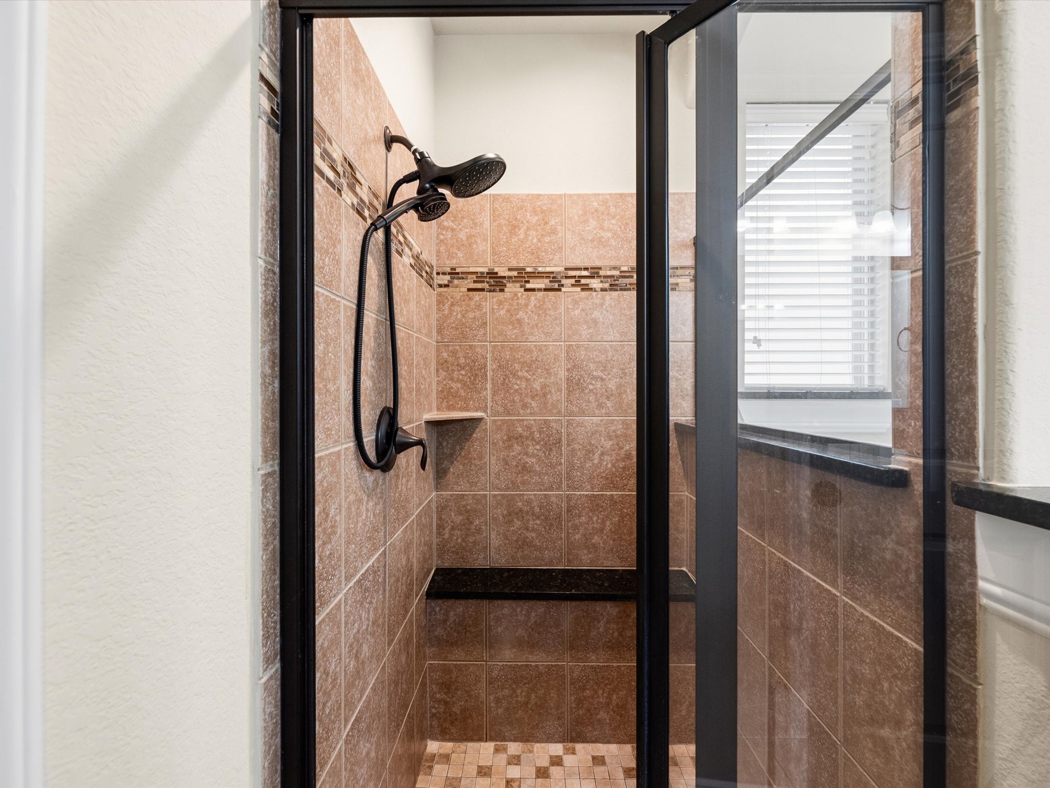 3907 Randle Ridge Court Fulshear, TX 77441 - Photo 21 of 46 This photo shows a modern shower with brown tile walls and a decorative mosaic border. It features a glass door, a built-in bench, and a sleek ORB showerhead.