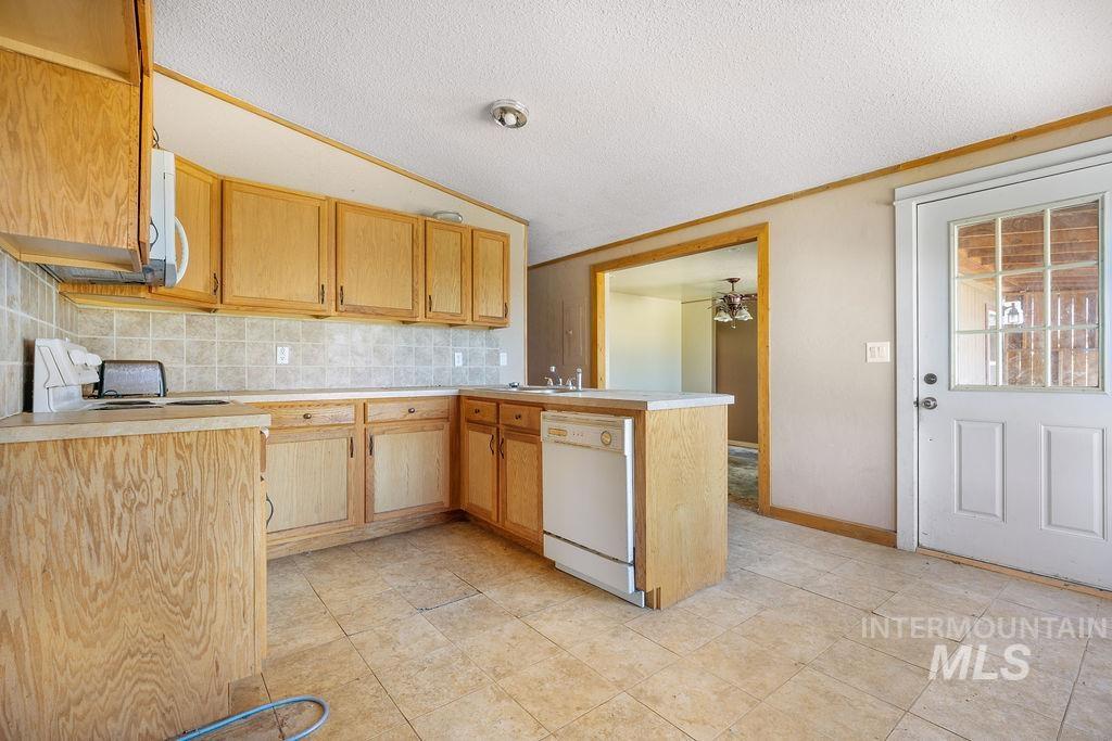 7370 Sagebrush Lane Caldwell, ID 83607 - Photo 24 of 40 Kitchen with light countertops, a peninsula, white appliances, backsplash, and light wood finish cabinets