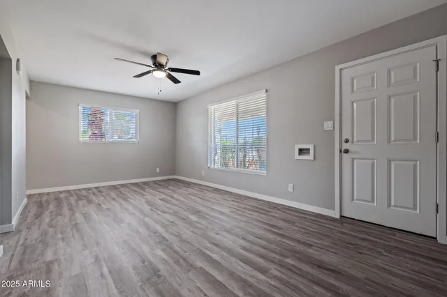 an empty room with wooden floor ceiling fan and windows