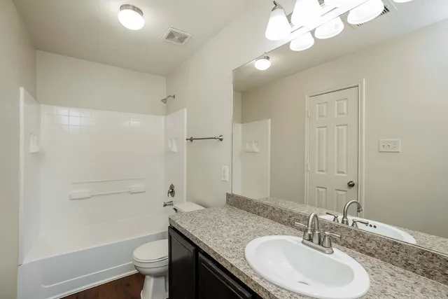 a bathroom with a granite countertop sink a toilet a mirror and shower