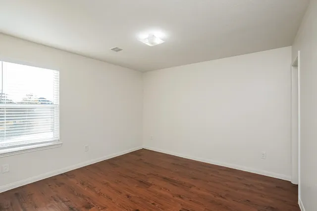 a view of an empty room with wooden floor and a window