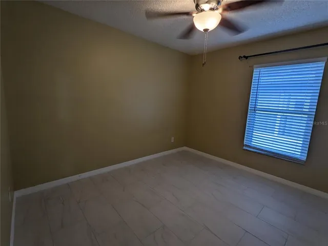 a view of an empty room with window and chandelier fan