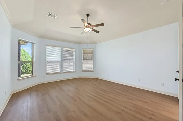 an empty room with wooden floor ceiling fan and windows