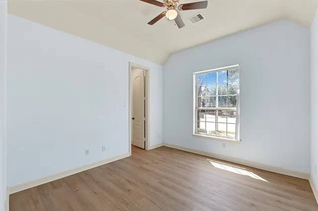 an empty room with wooden floor fan and windows