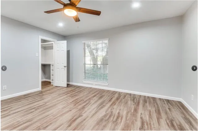 an empty room with wooden floor fan and windows