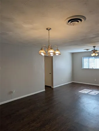 an empty room with wooden floor chandelier and windows