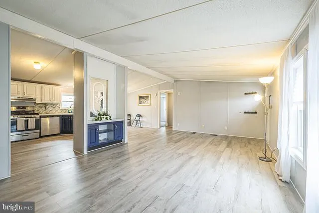 an empty room with wooden floor and kitchen view