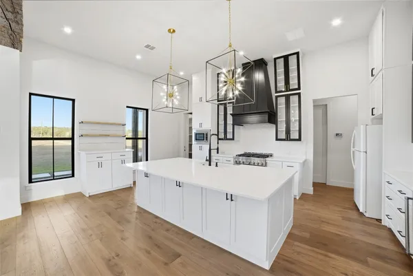 a large white kitchen with stainless steel appliances kitchen island granite countertop a stove a refrigerator a oven and a sink with large countertops