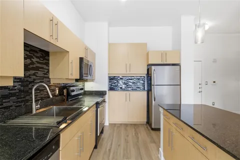 a kitchen with stainless steel appliances granite countertop a refrigerator a stove and a sink with wooden floor